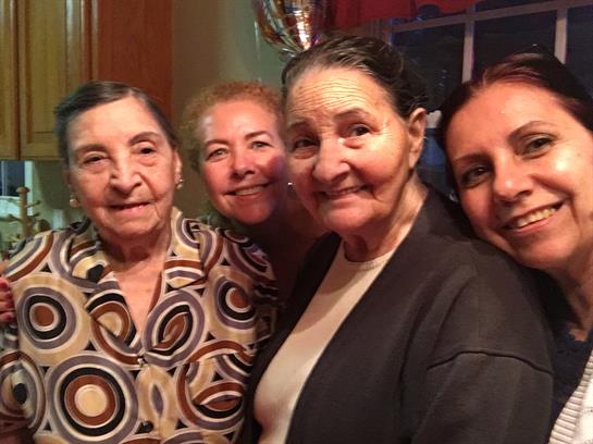 Four women smile warmly as they pose together at a family gathering, showcasing their close bond.