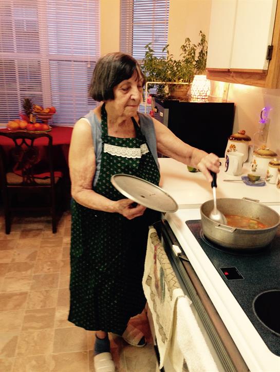 An elderly woman stirs a pot on the stove, preparing a cherished family meal in her warm kitchen.