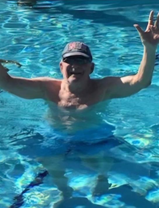 A shirtless man raises his arms in excitement while enjoying a sunny day in a pool.