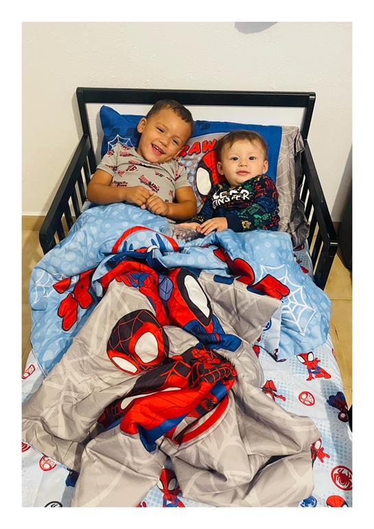 Two boys are lying in a bed covered with Spider-Man blankets, smiling and having fun.