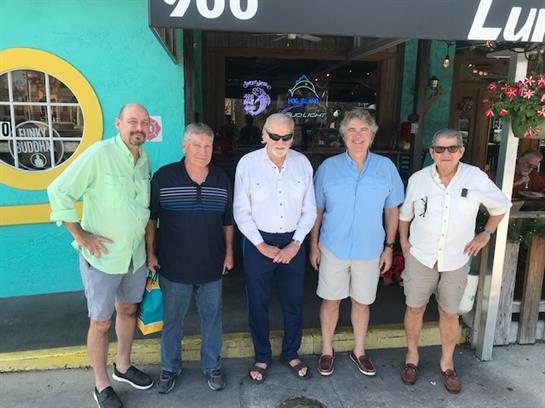 Five men stand cheerfully outside a vibrant cafe, showcasing friendship and relaxation.