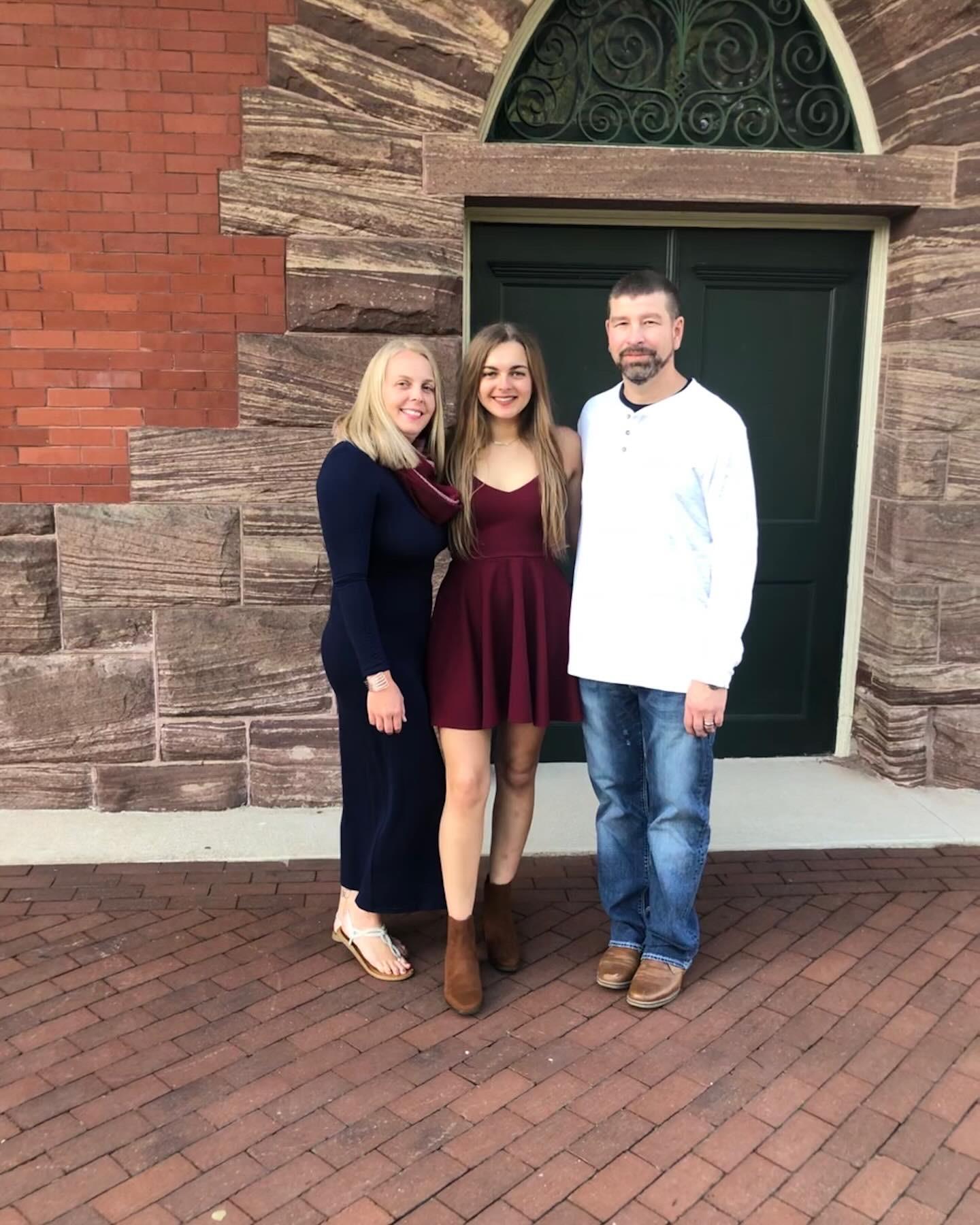 Family members stand together smiling at a historic location on a sunny afternoon.