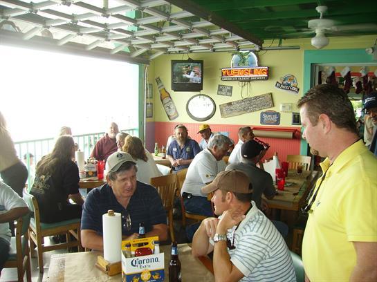 Diners gather in a lively waterfront restaurant, enjoying food and drinks while chatting.