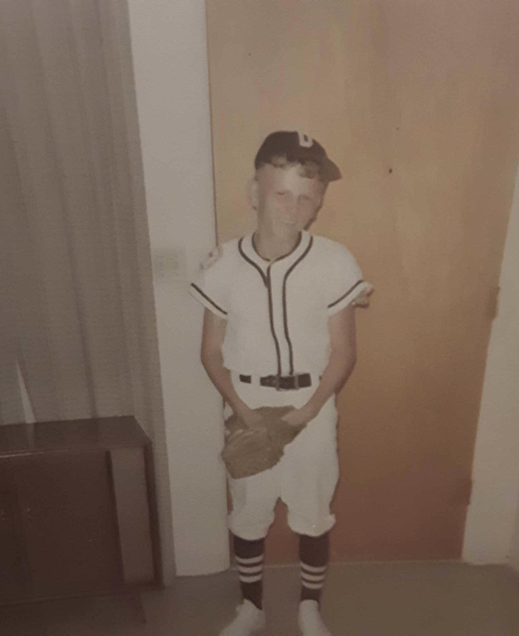 A young athlete stands in uniform with a baseball glove, showcasing dedication to the sport.