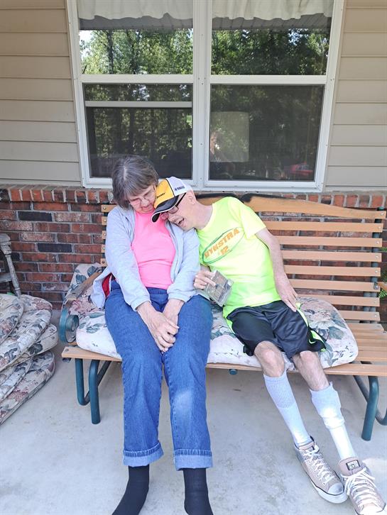 Two people sit closely on a bench enjoying time together in a residential area outside.