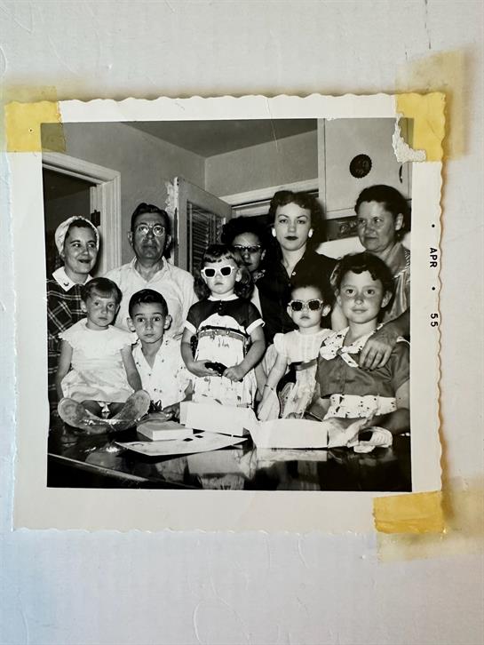 A group of adults and children gathering around a table, all dressed in 1950s styles.
