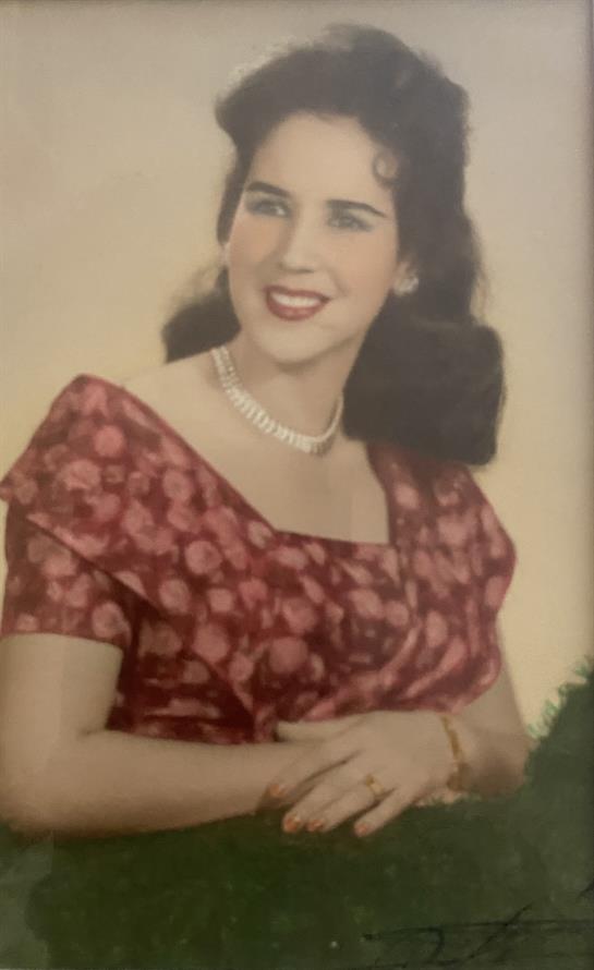 A smiling woman poses gracefully in a floral dress and pearl necklace, exuding charm.