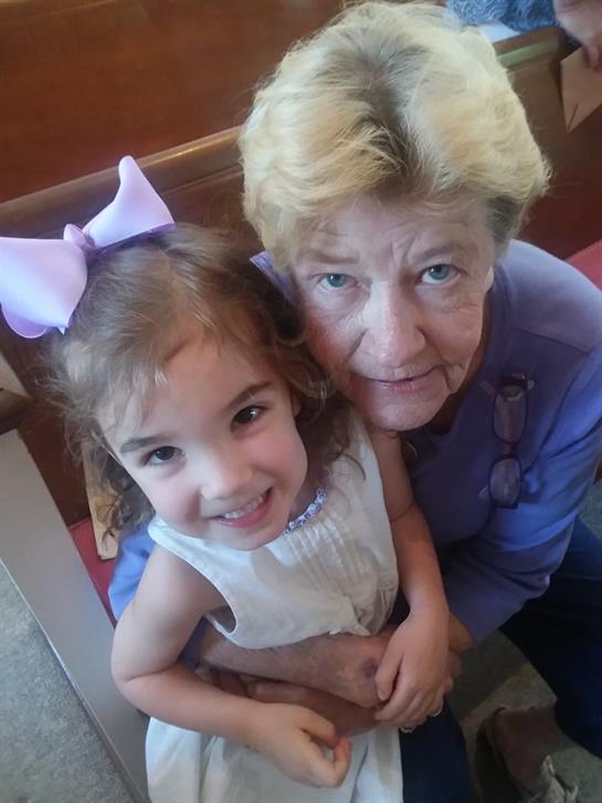 A girl with a large bow smiles while hugging her grandmother in a church.