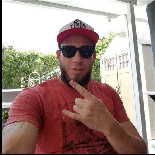 A man poses confidently with sunglasses and a cap, enjoying a relaxed moment outside.