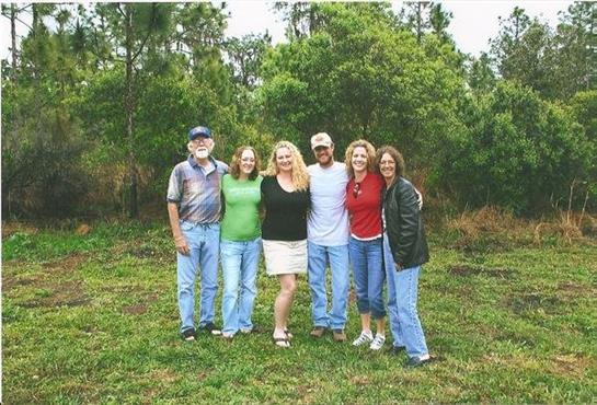 Six friends smile together in a lush green area, enjoying their time outdoors.