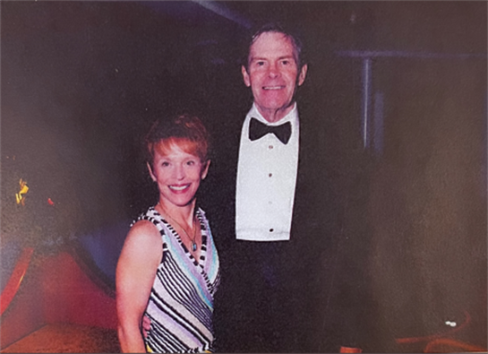 Two individuals dressed elegantly are posing together at a festive gathering indoors.