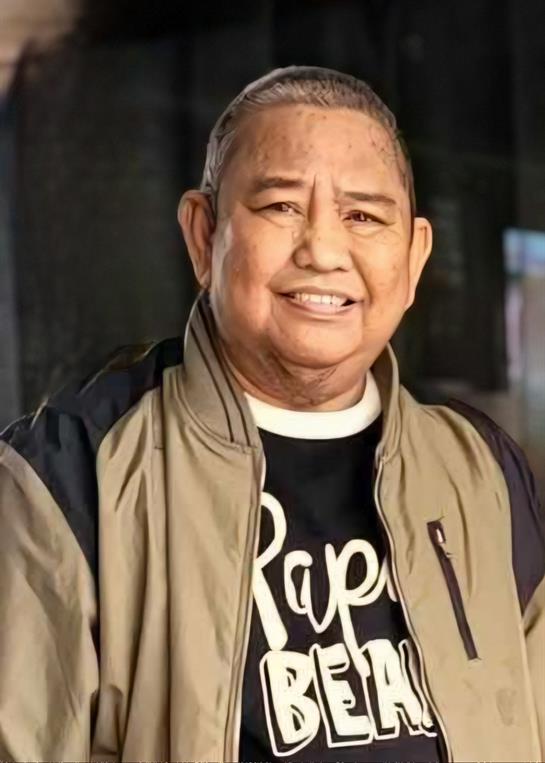 Elderly man smiles warmly while dressed in a jacket and graphic t-shirt, radiating happiness.