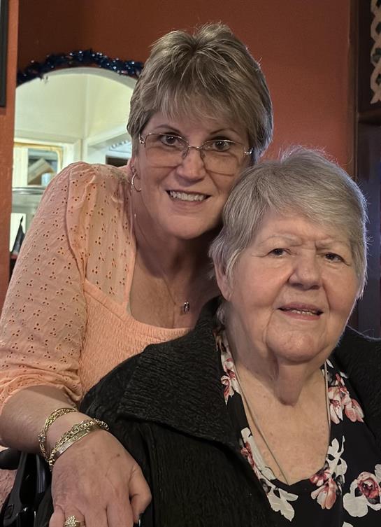 Two women smile warmly at each other while sitting together in a friendly home environment.