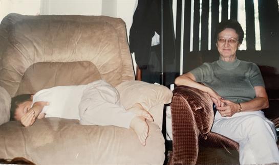 A child snuggles on the couch as Grandma watches with a warm smile.