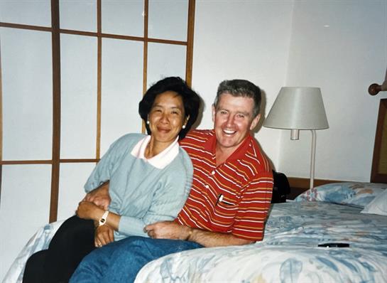 Two people sit closely on a bed, sharing smiles and enjoying each other's company in a hotel.