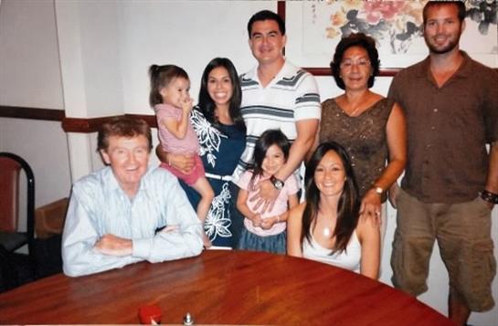 A group of seven people gathered around a wooden table, smiling and enjoying each other's company.