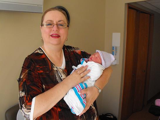 A woman smiles while gently cradling a newborn wrapped in a blanket.