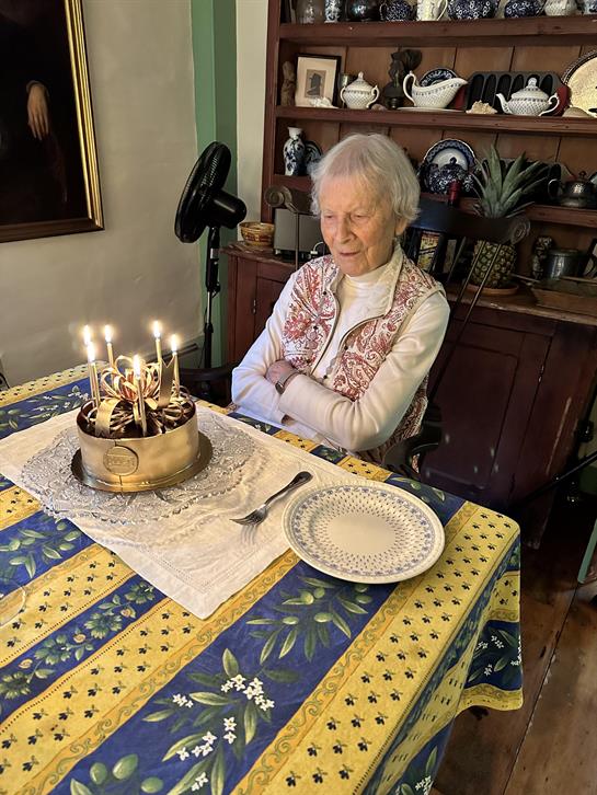 An old woman sitting at a table with a cake with lit candles