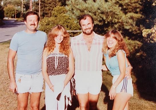 Four friends gather together on a warm day, smiling and dressed in retro summer apparel.