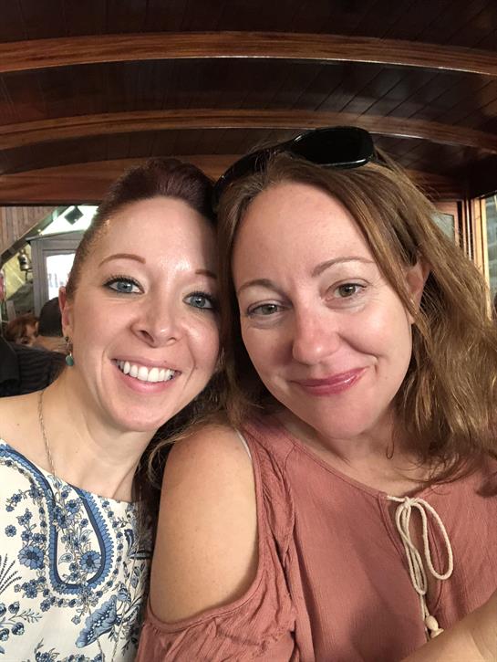 Two women are smiling together in a warm, inviting atmosphere, showing friendship and joy.