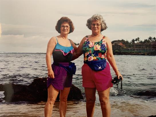 Two women stand on the shore, smiling and ready for a fun day by the sea with rocky coastline.