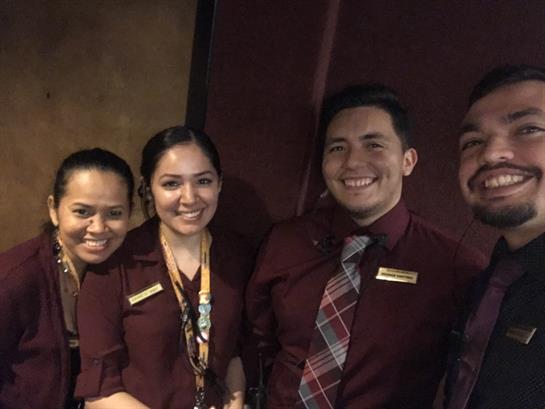 Four hospitality professionals stand together smiling in a relaxed indoor setting.