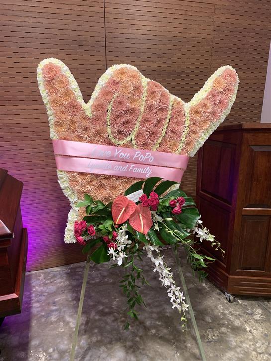 A large flower arrangement resembling a hand gesture stands in tribute at a memorial service.