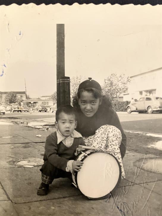 Two children are happily playing with a drum on a sunlit street in a historic neighborhood.