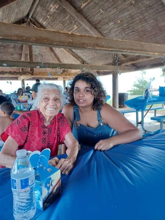Two family members share a warm moment at a seaside location with blue tables and smiling faces.