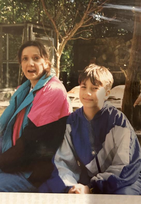 A mother and her son sit together, smiling in a joyful moment at a family gathering outside.