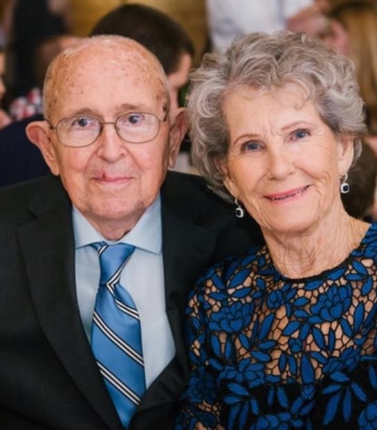 A couple enjoys a joyful moment at a formal gathering, surrounded by friends and family.
