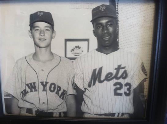 Two young athletes in baseball uniforms stand side by side, smiling at a training facility.