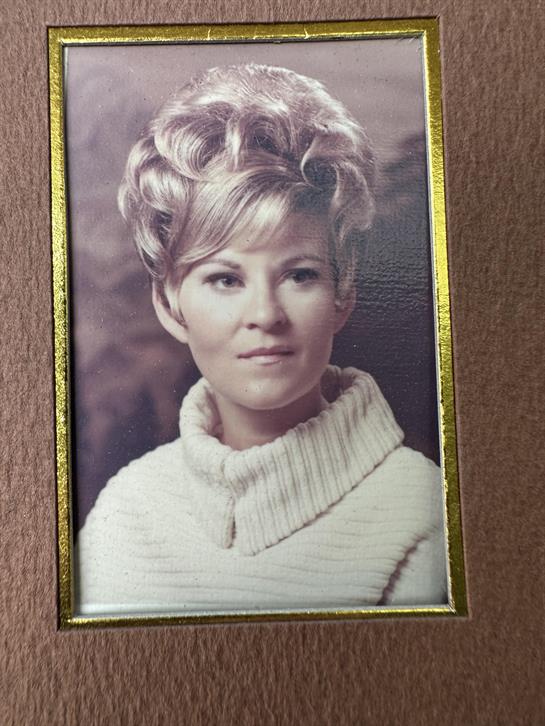 A woman with elegantly styled hair poses in a cozy sweater, evoking a sense of nostalgia.