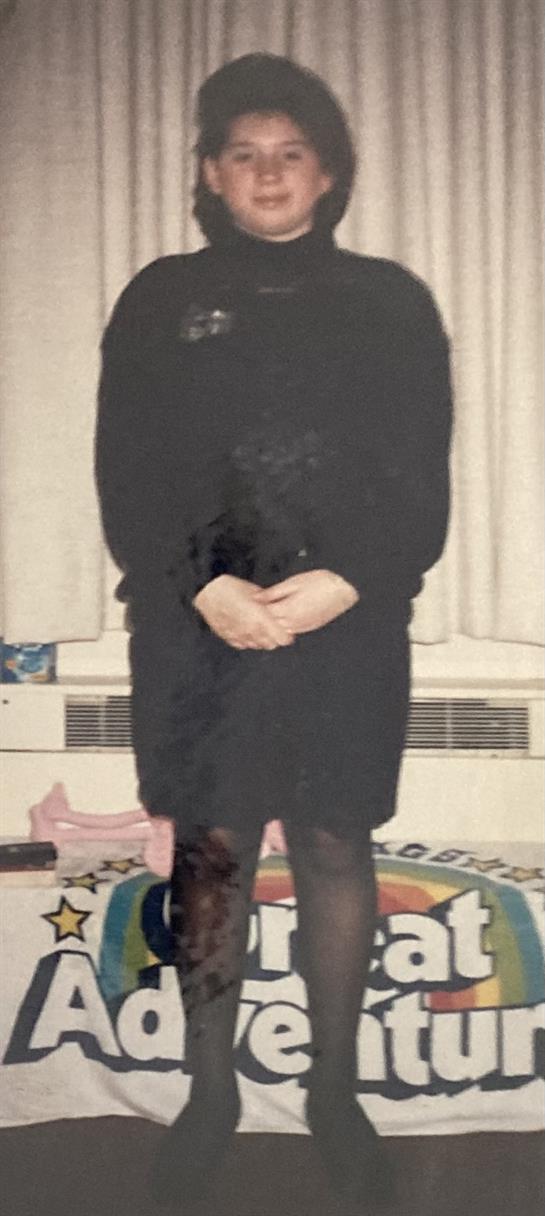 A young woman poses with a smile at an event, wearing a stylish all-black outfit.