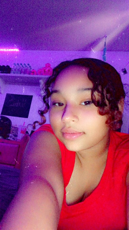 A cheerful girl poses for a selfie in her lively room filled with colorful lighting.