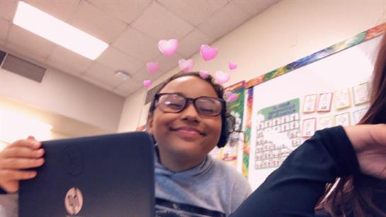 A cheerful student wears headphones and smiles while using a laptop in class.