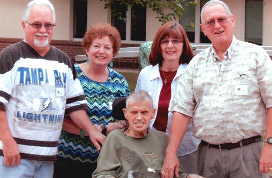 A joyful family gathering takes place outdoors with an elderly man in a wheelchair.