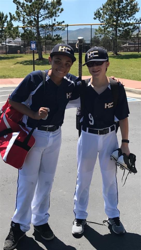 Two boys wearing baseball uniforms and holding shoes