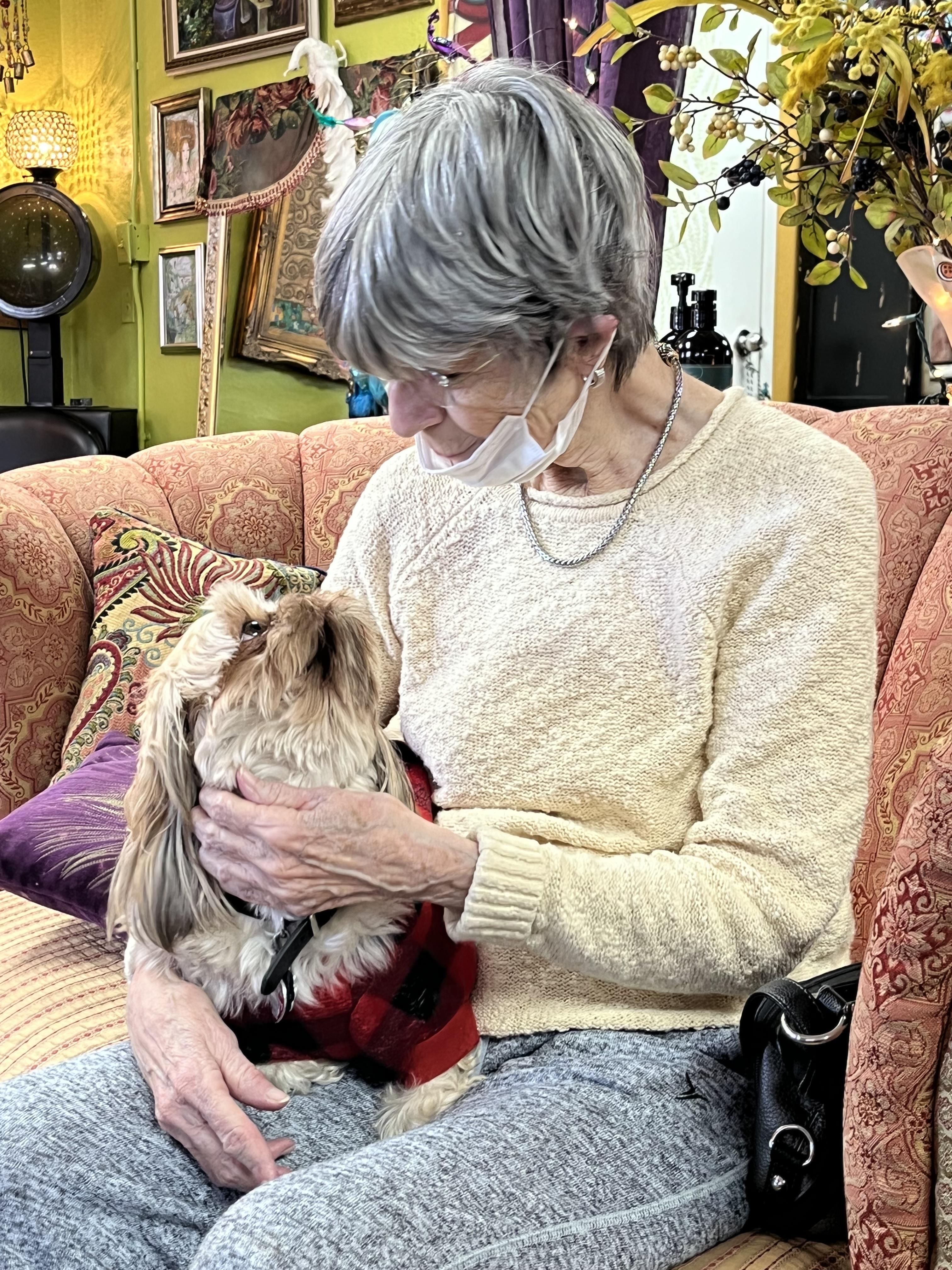 An older woman sits on a comfortable couch interacting lovingly with her small dog.