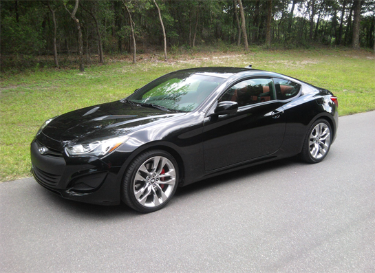 A sleek black coupe is parked on a winding road with a lush green backdrop.