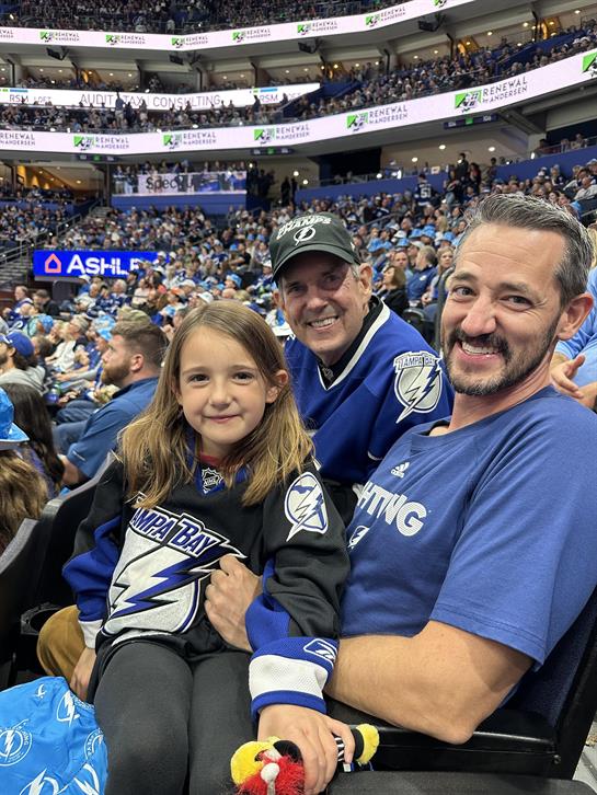 Excitement fills the air as a family of three cheers enthusiastically for their hockey team.