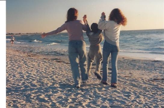 Three people are playing together on a sandy beach as the sun sets over the ocean.