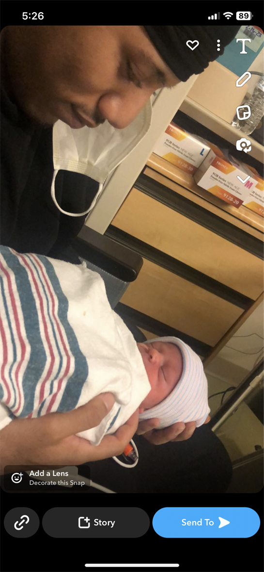 A joyful father holds his newborn baby swaddled in a striped blanket in a hospital room.