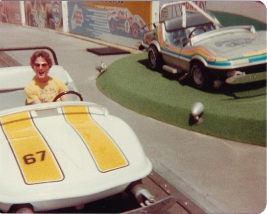A child is seated in a go-kart at a funfair, smiling as they prepare for a joyful ride.