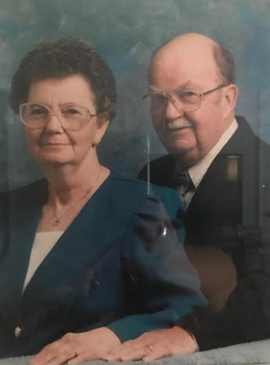 An elderly couple smiles warmly while dressed in formal attire, highlighting their enduring love.
