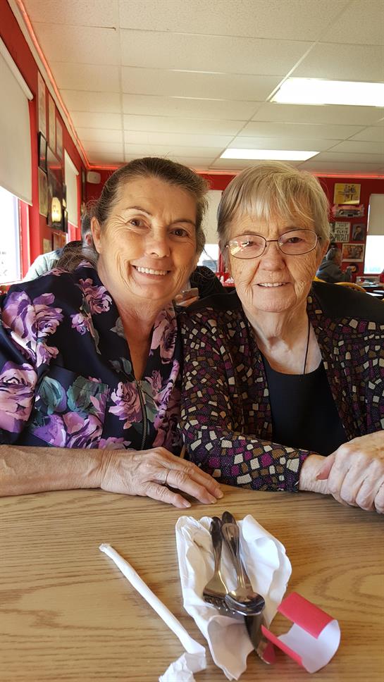 Two women smile warmly as they sit together at a cozy diner, sharing a precious moment.