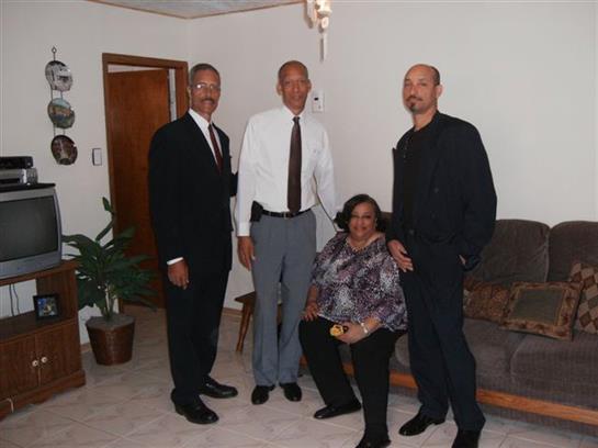 Four adults dressed formally converse while standing and sitting in a living room.