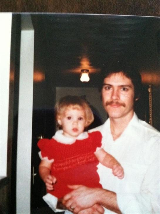 A father embraces his young daughter in a warmly lit, intimate indoor environment.