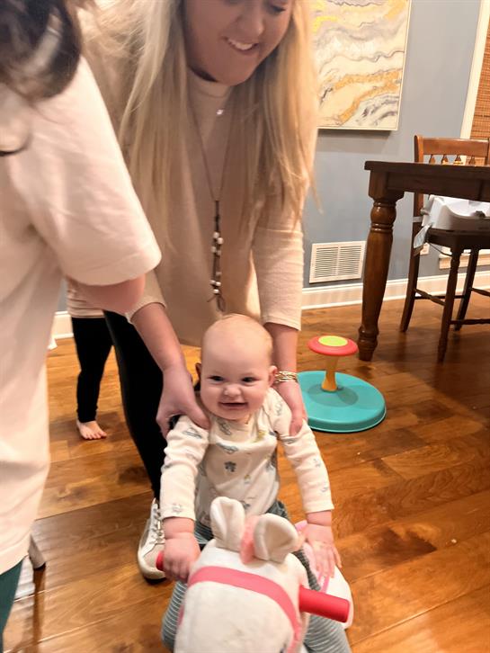 A cheerful baby is being helped by a caregiver while playing with a toy.