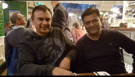 Two men sit comfortably at a table, sharing laughter and conversation in a lively restaurant.